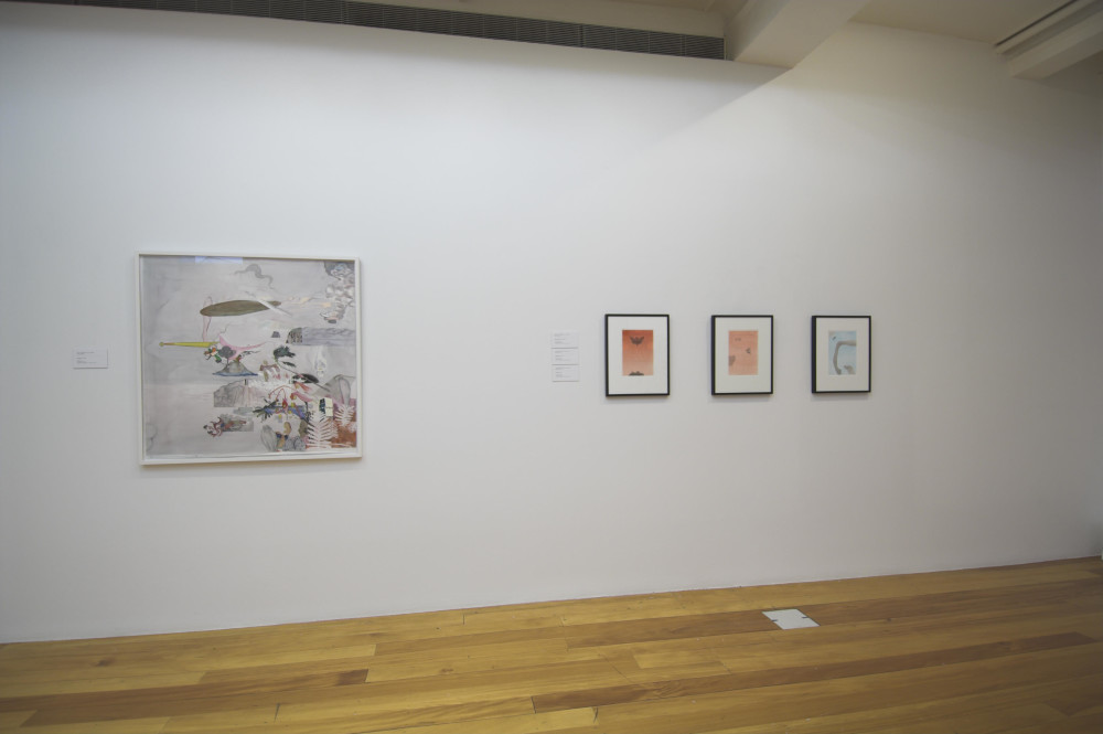 The image shows a white gallery wall with a polished wooden floor. On the left hand side of the wall is a large framed square watercolour artwork showing a clustered arrangement of random objects, motifs and patterns against a murky grey background. On the right hand side three small, portrait artworks with black frames are arranged in a row, each showing a bird's silhouette above an orange gradient, a faint outline of a cat against an orange gradient, and a bird flying towards the vague outline of a person's face, away from a horse's bent leg with curled hoof and a dog gazing upwards towards it.